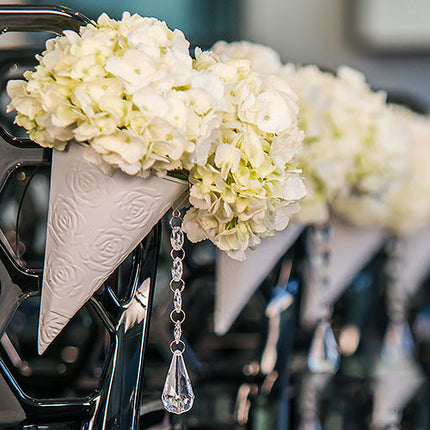 White Metal Cone filled with flowers that line a wedding aisle.